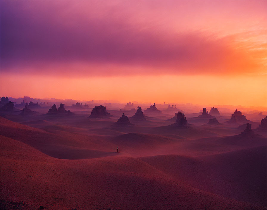 Solitary figure in desert at sunset with purple and orange sky