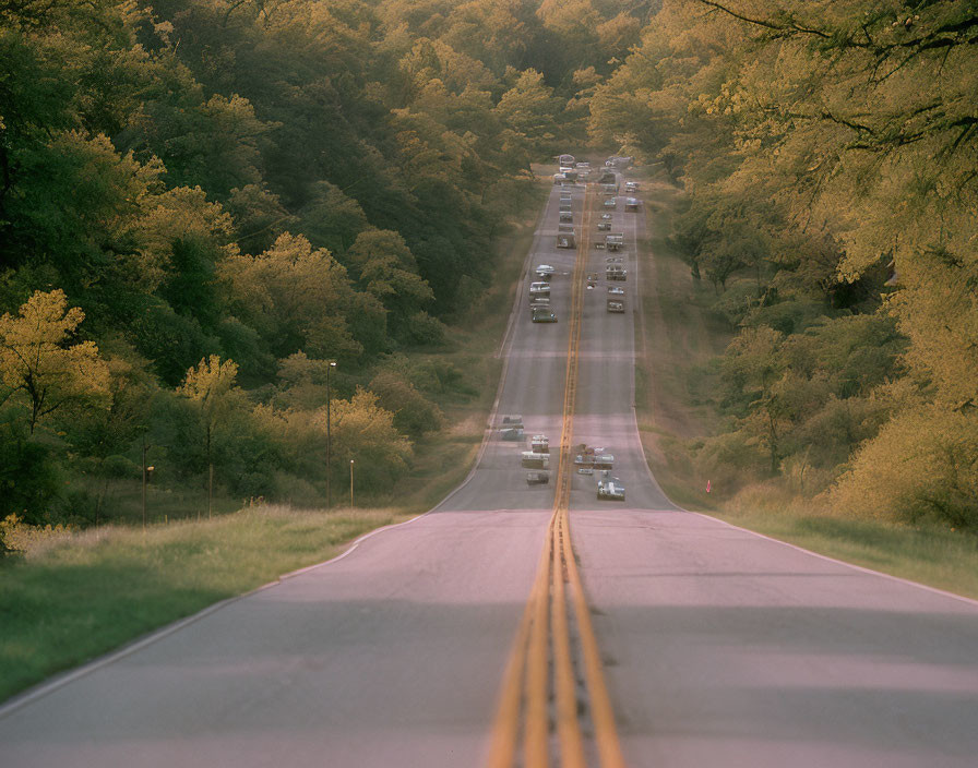 Two-lane road in lush green landscape with vehicles and double yellow line