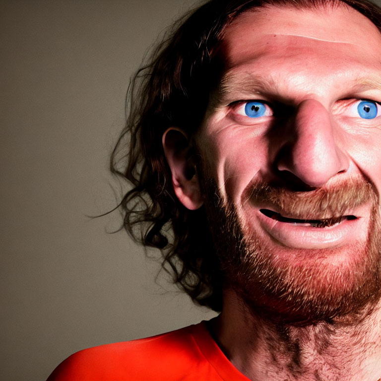 Smiling man with blue eyes, curly hair, and beard on grey background