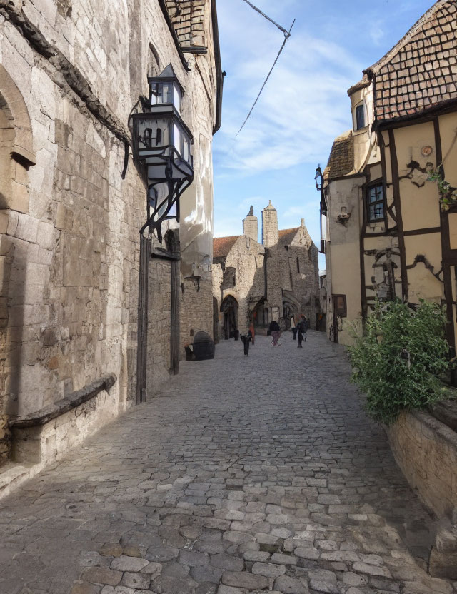 European-style cobblestone street with old buildings, lanterns, and pedestrians under clear sky