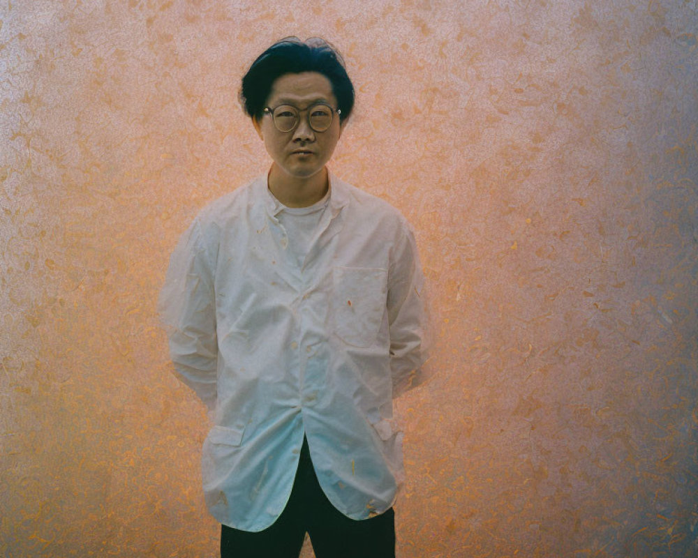 Man in white shirt and glasses against amber background