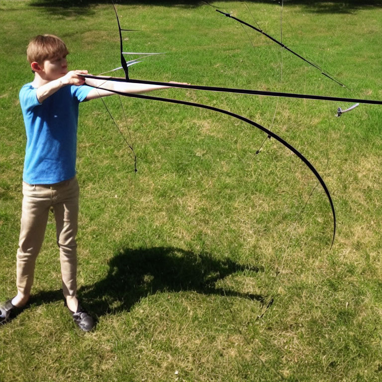 Boy in blue shirt aiming bow in sunny field