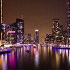 Twilight cityscape with illuminated skyscrapers, waterfront, palm trees, and crescent moon eclipse