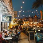 Colorful painting of New Orleans street at dusk with cathedral, strolling people, and plant-adorn