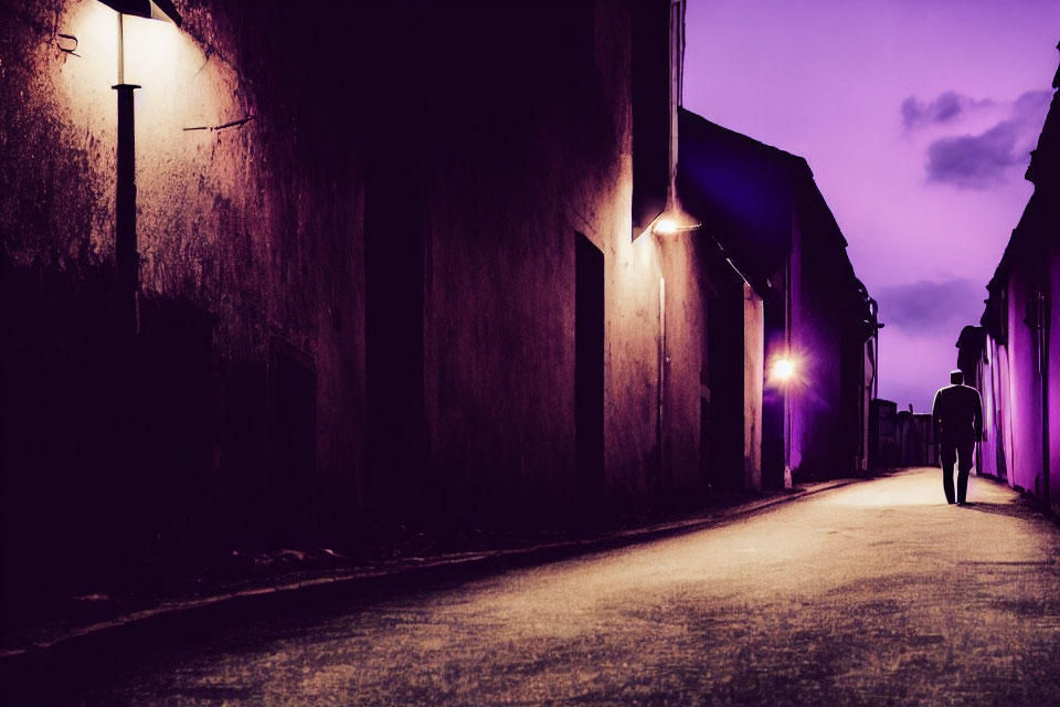 Silhouette of person walking on dimly lit street at twilight