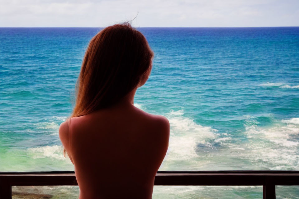 Woman gazing at tranquil blue sea from balcony