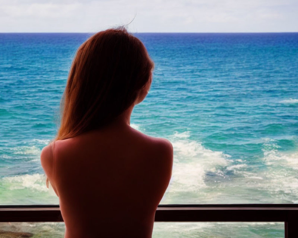 Woman gazing at tranquil blue sea from balcony