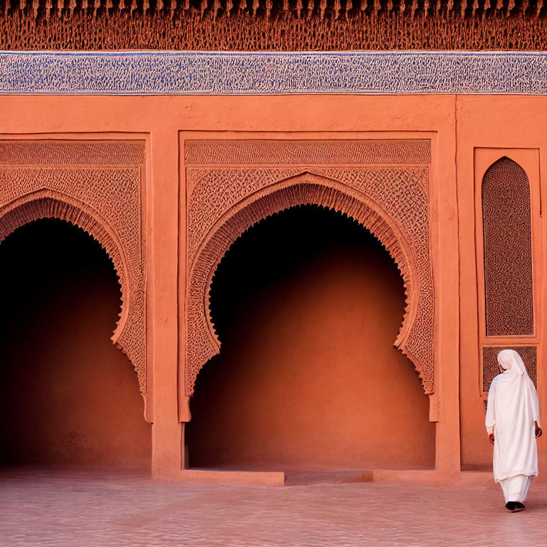 Person in White Traditional Attire Walking Past Ornate Arched Doorways