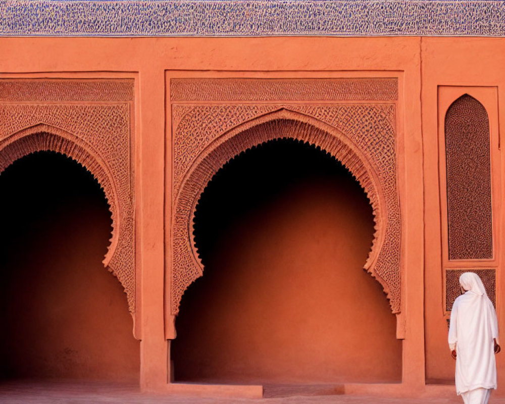 Person in White Traditional Attire Walking Past Ornate Arched Doorways