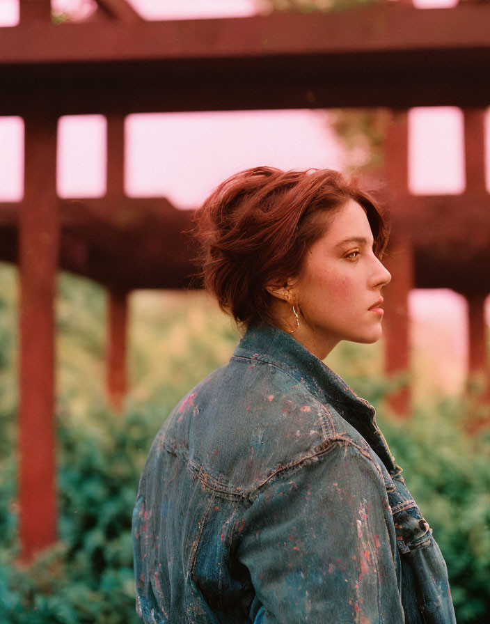 Woman in denim jacket against red-toned background with wooden beams