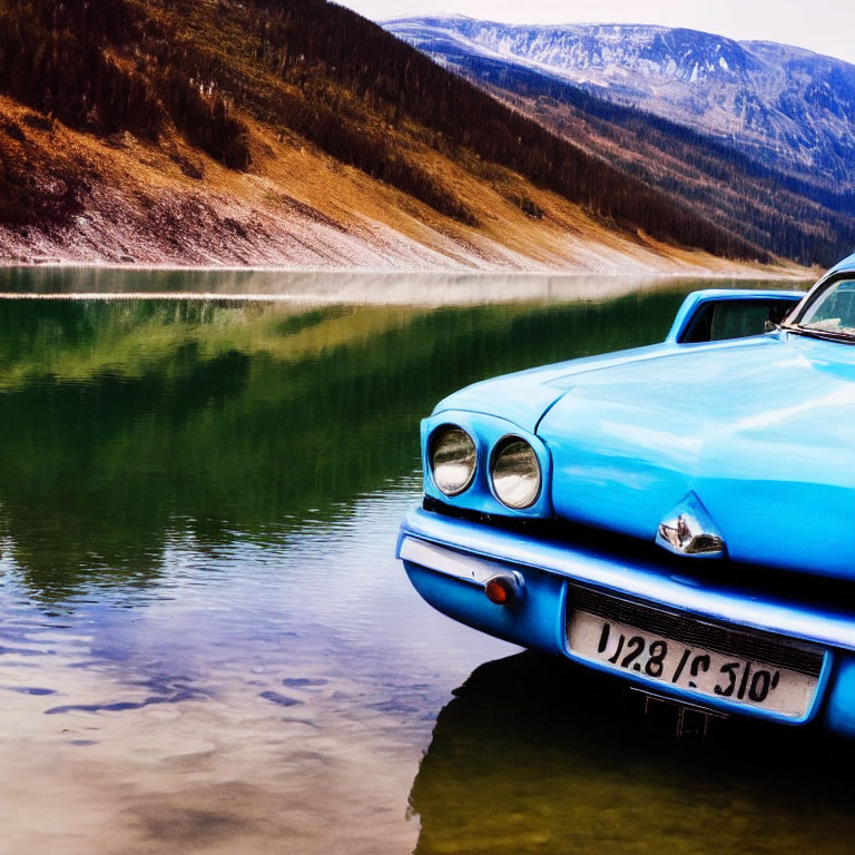 Vintage blue car by serene lake with forested hills & mountains