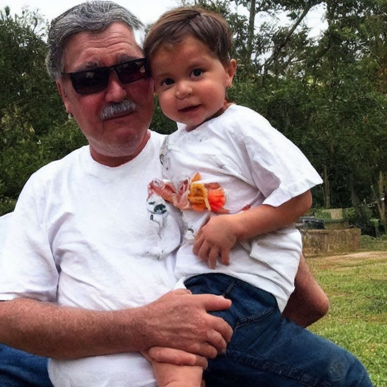 Elderly man with sunglasses holding child in park