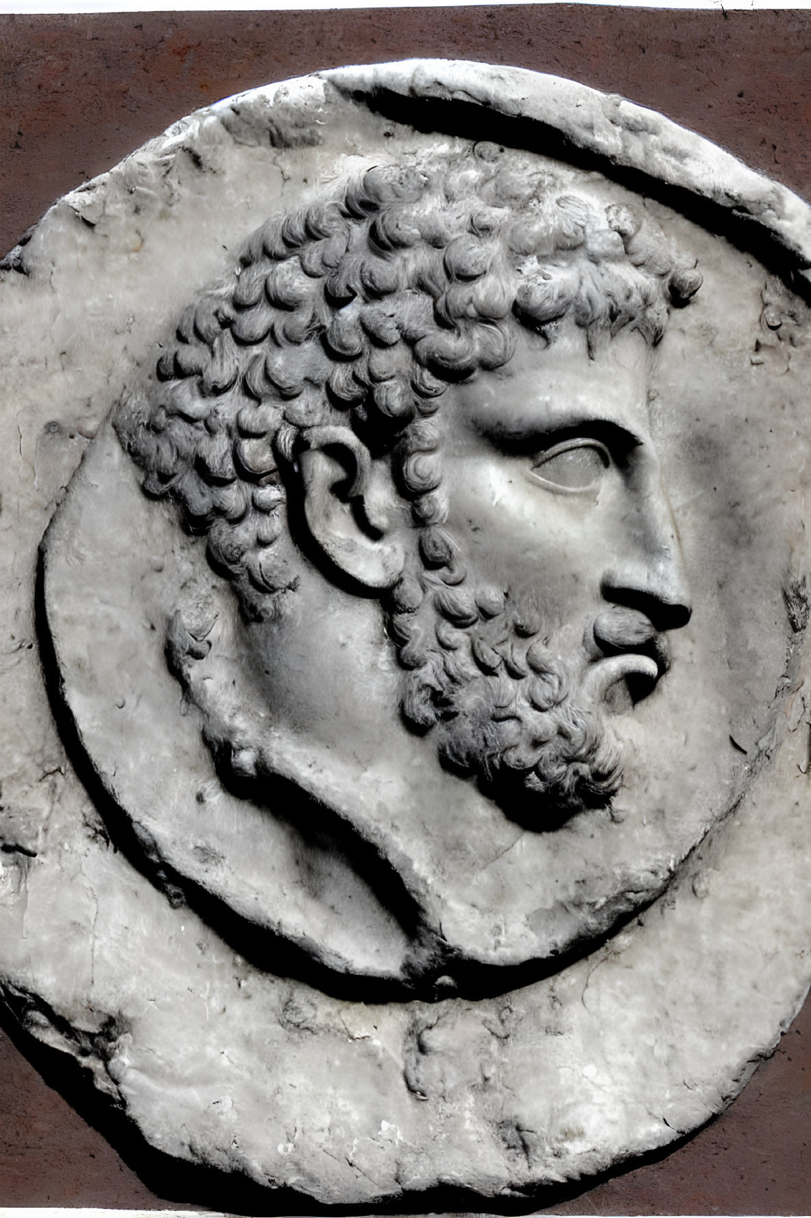 Ancient bas-relief sculpture of a bearded male with intricate hair and facial features.