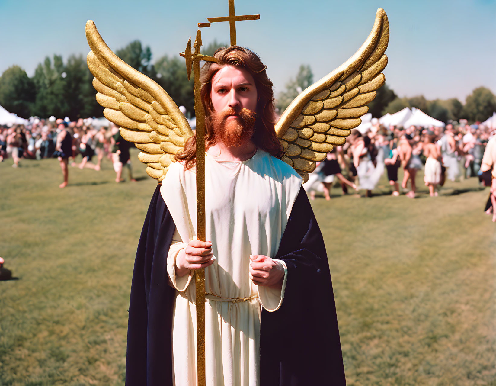 Person in angel costume with golden wings and cross in sunny field.