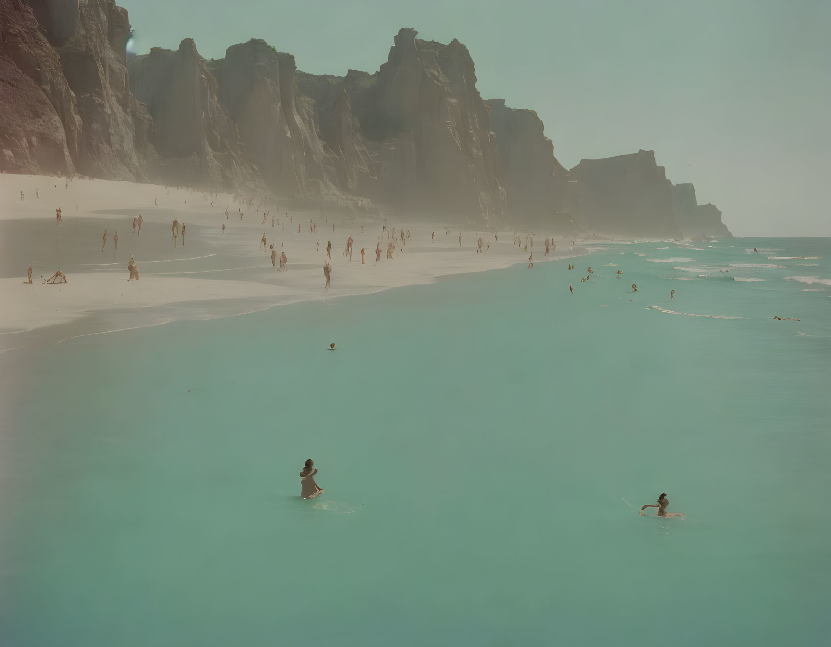 Turquoise waters and cliffs frame a busy beach scene