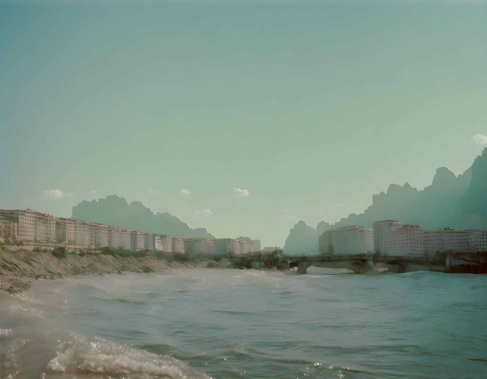 Scenic river with buildings, mountains, and blue sky