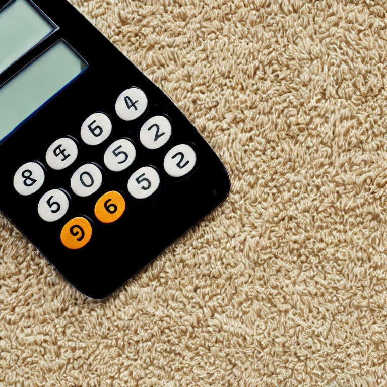 Black Calculator with Orange Stickers on Number 9 Button on Beige Shaggy Carpet