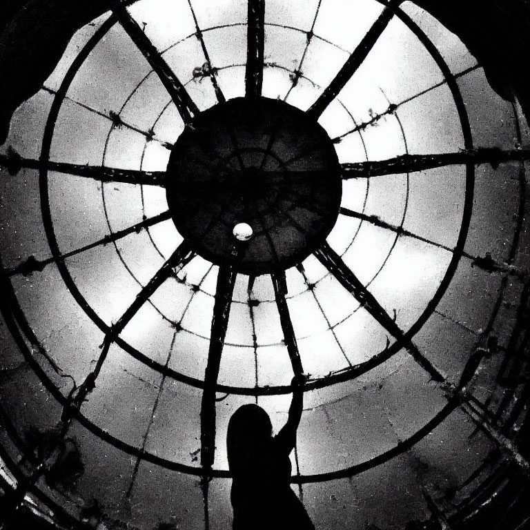 Person silhouette under geometric dome with radial patterns and hanging light in black and white.