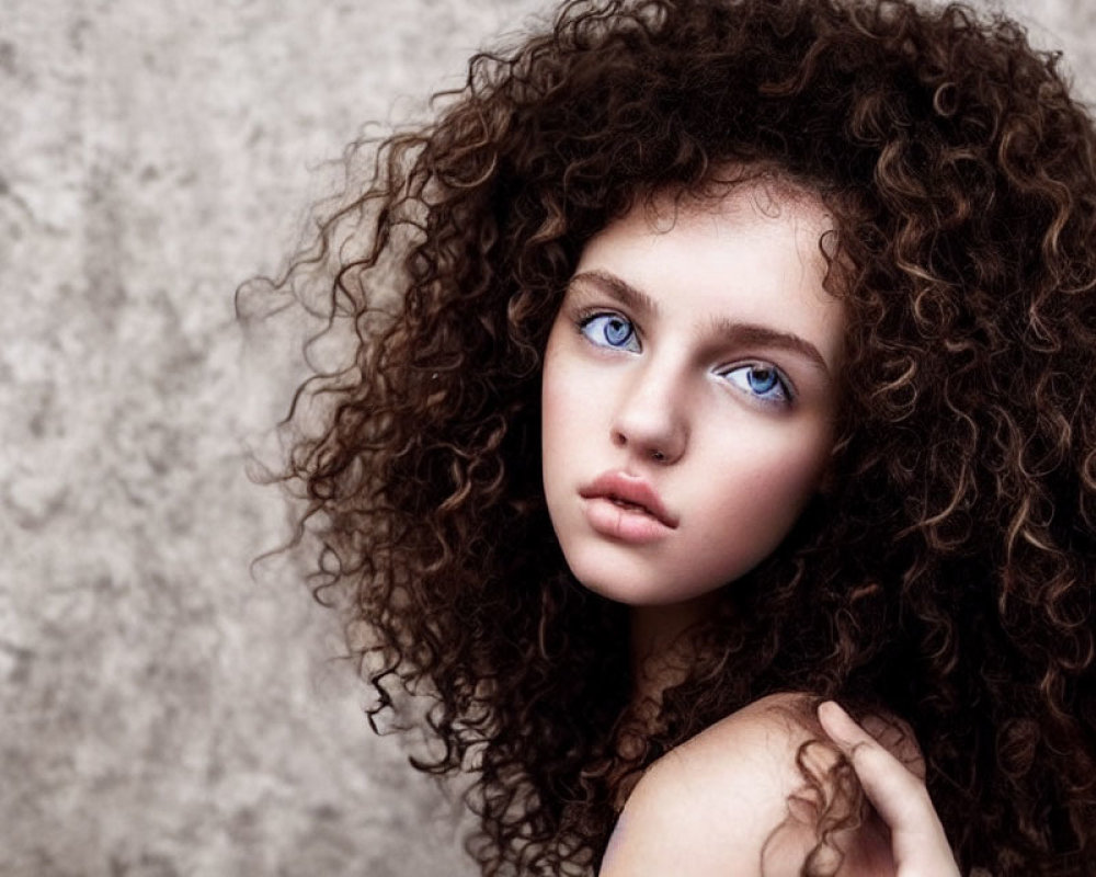 Young woman with voluminous curly hair and striking blue eyes against neutral textured backdrop