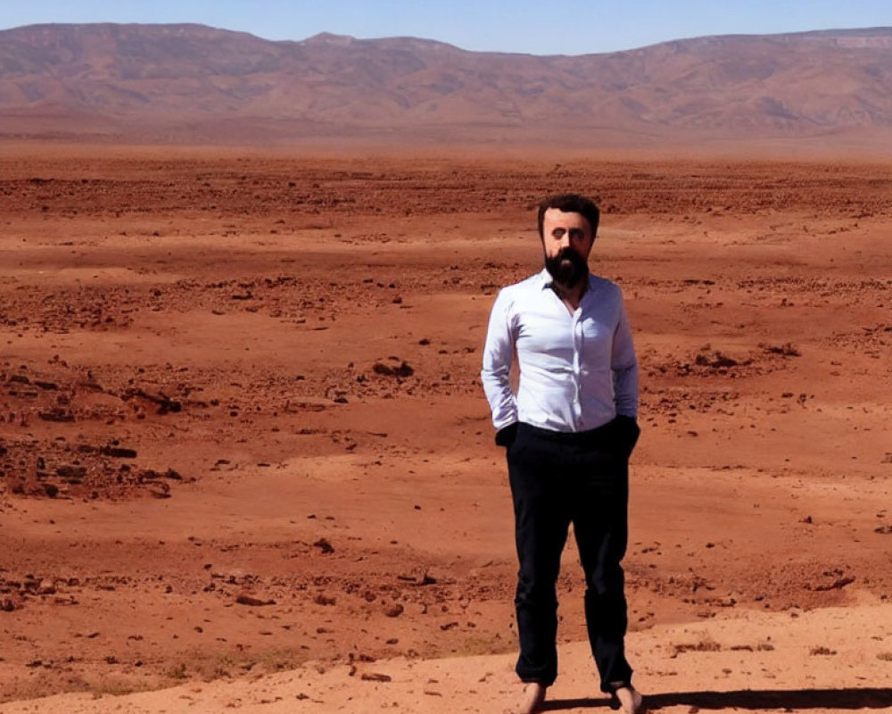 Bearded man in white shirt and black pants on red desert landscape