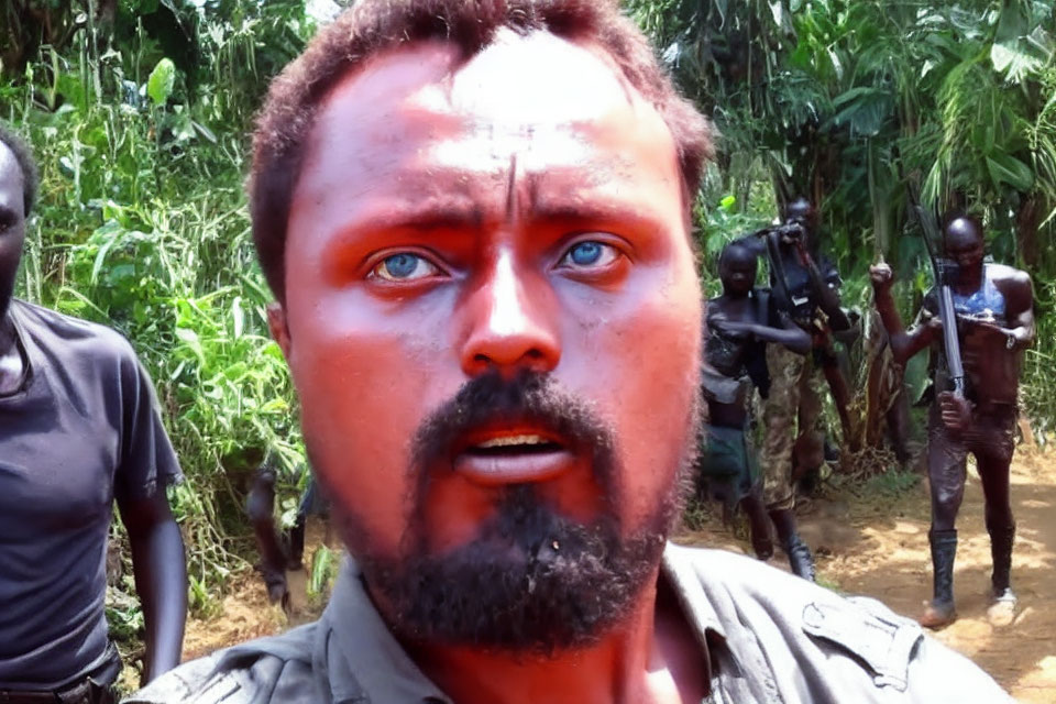 Blue-eyed man with face paint shocked by armed individuals in forest setting