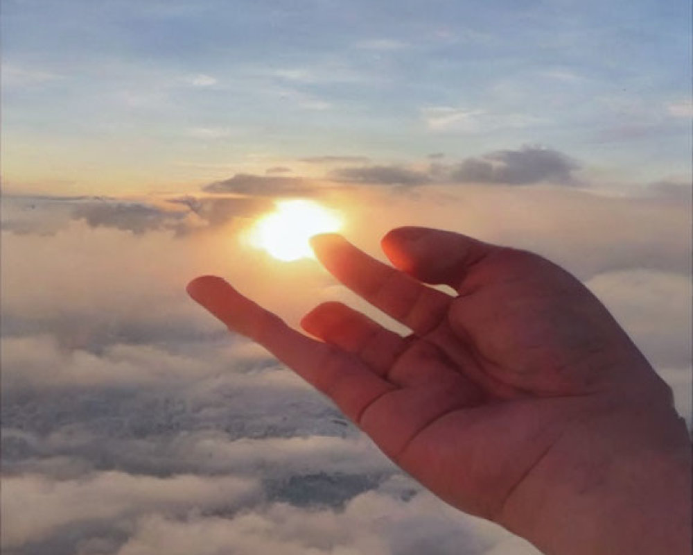 Silhouetted hand against cloudy sky with sunlight diffusing.