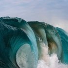 Towering Wave with White Foam Against Blue Sky