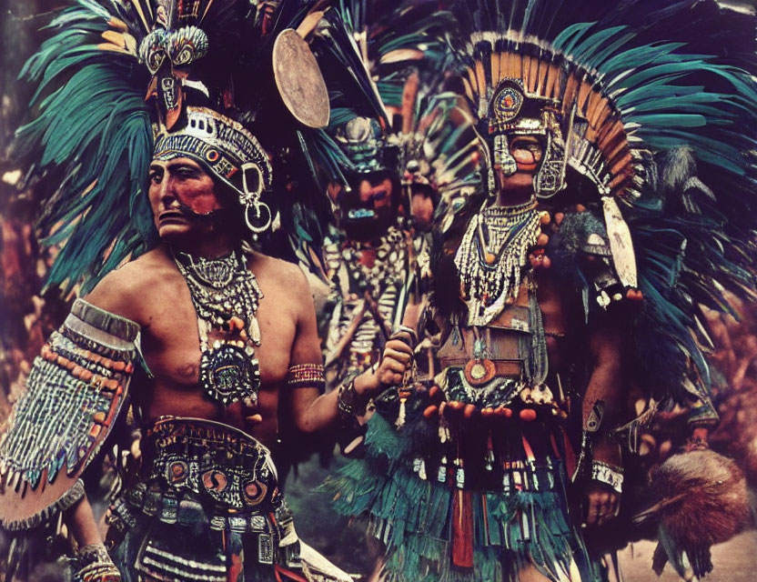 People in traditional indigenous attire with feathered headdresses and drum.