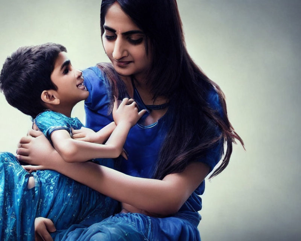 Young boy in blue kurta gazes at woman in traditional Indian attire