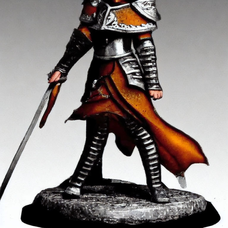 Miniature knight figurine in plate armor with red cape and sword on rocky base