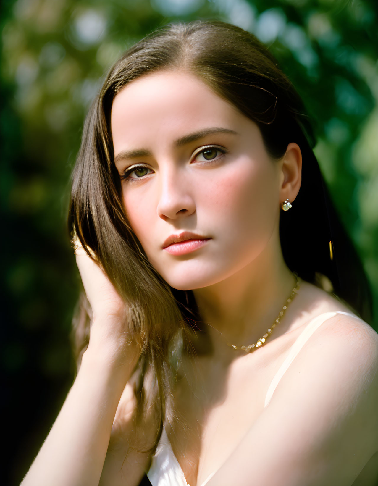 Young woman with dark hair in dreamy pose outdoors.