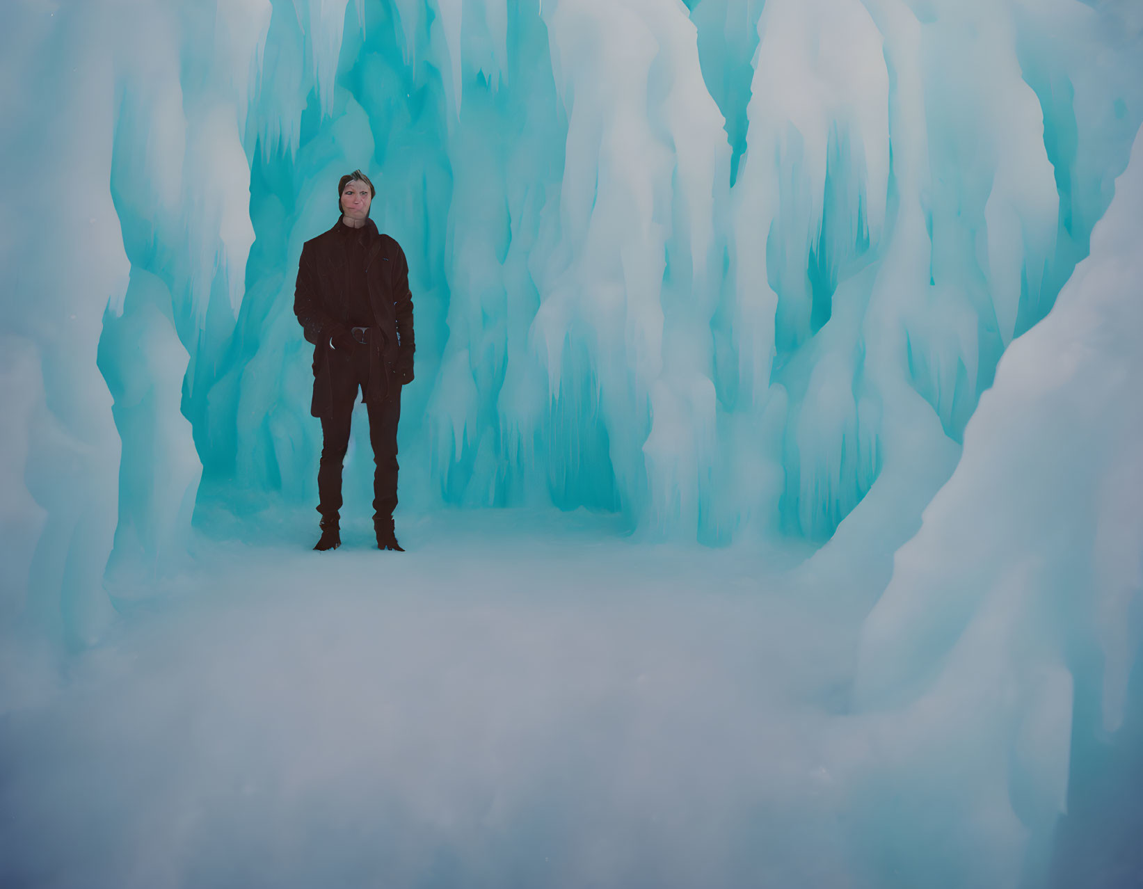 Person in Black Clothing Stands in Cave with Blue Ice Walls