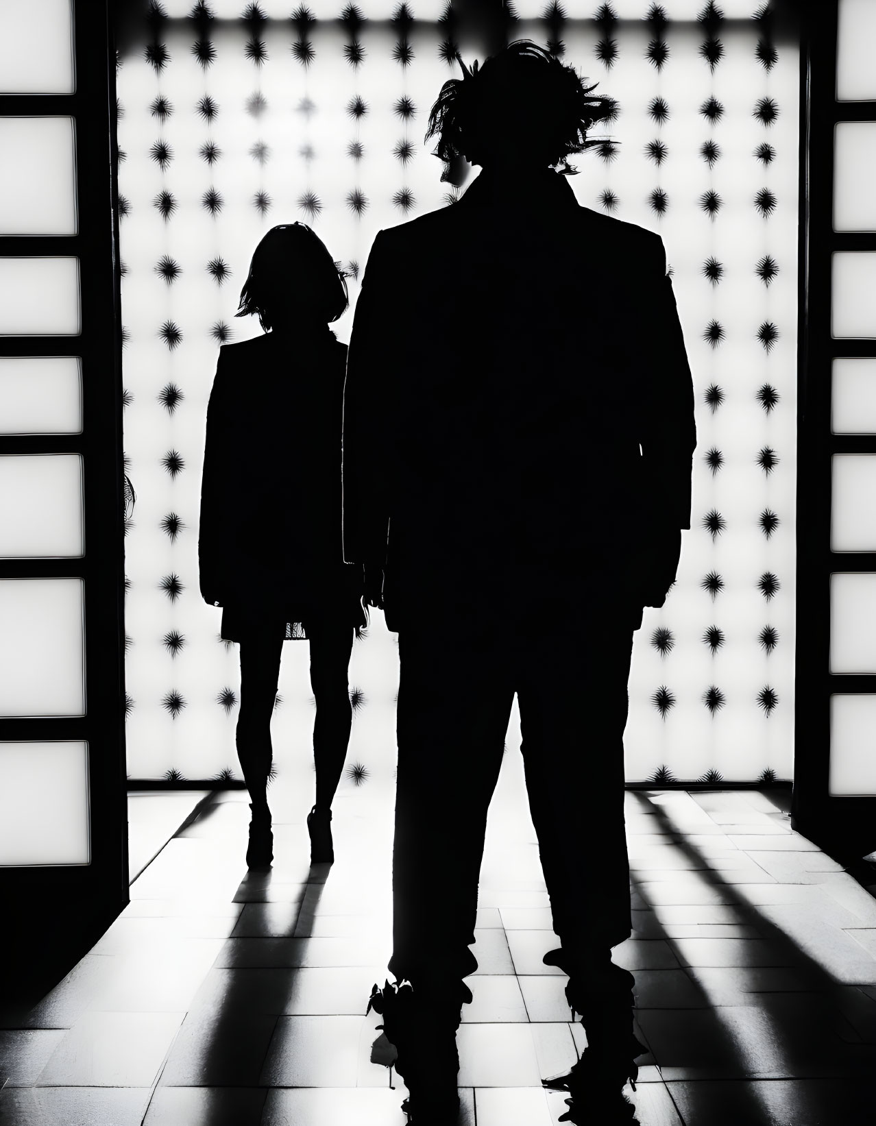 Man and woman silhouettes in high-contrast lit space with patterned backlit wall