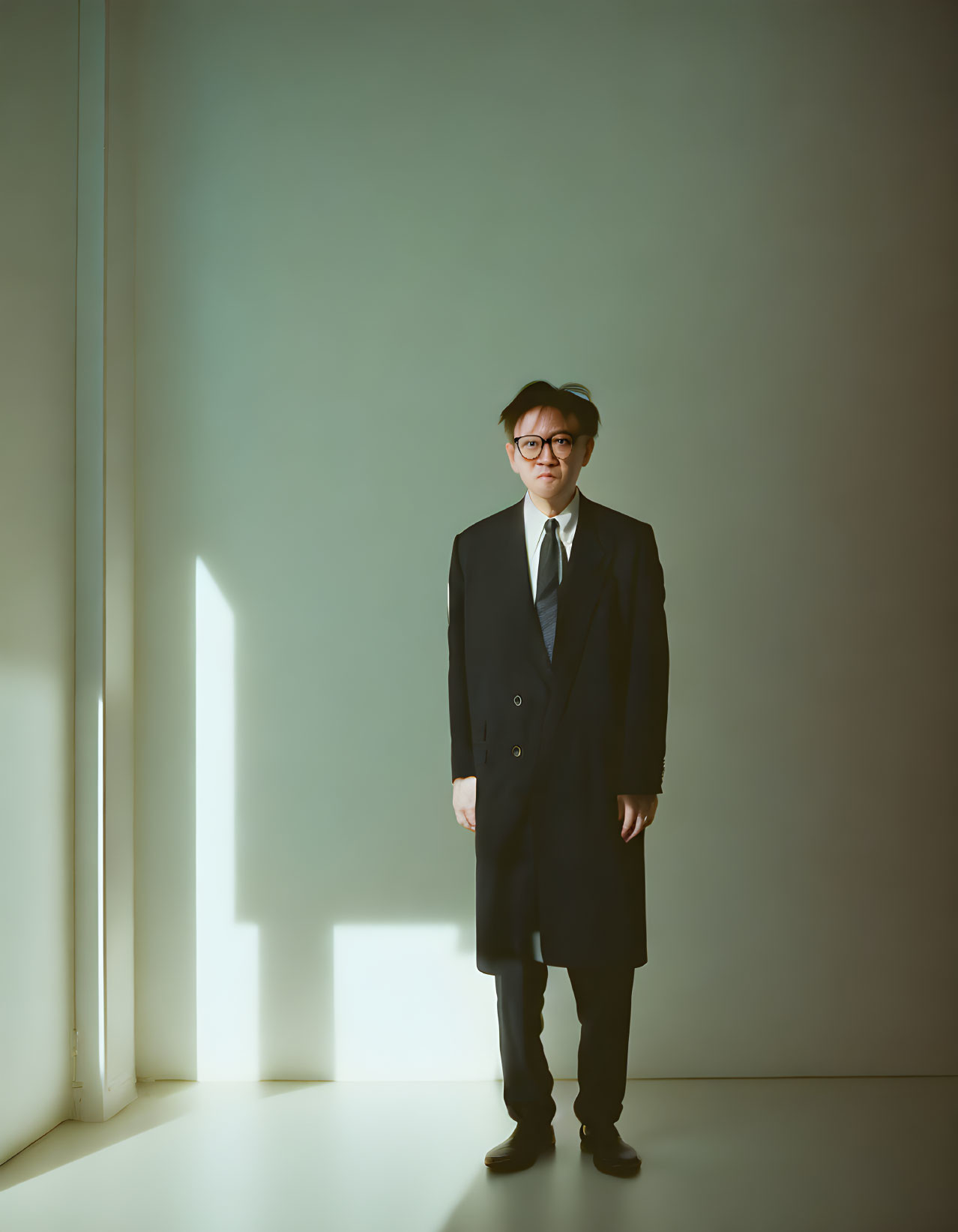 Man in dark suit and tie casting long shadow in softly lit room