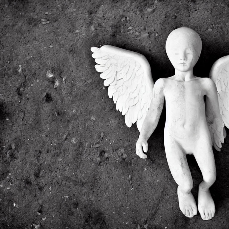 Small Winged Stone Statue Resting on Rough Textured Ground in Black and White