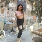 Woman in beige crop top at cozy café with green plants and hanging decorations.