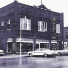 Vintage-style illustration of street corner with classic cars and restaurant building.