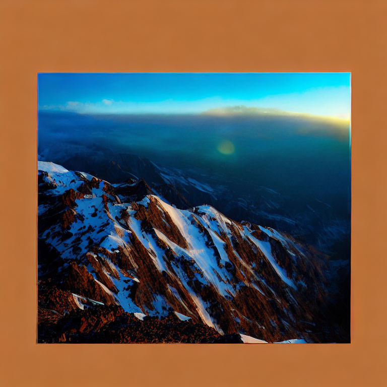 Snow-covered mountain range at sunset with orange light against deep blue sky