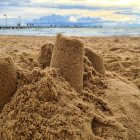 Elaborate sandcastle with towers and walls on beach under cloudy sky