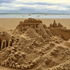 Detailed Sandcastle on Beach with Ocean View and Person Sitting in Background