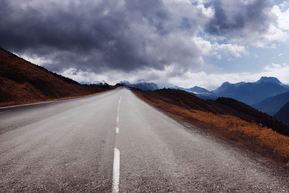 Dramatic sky over empty mountain road with autumn foliage