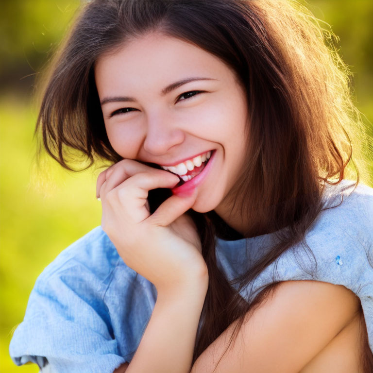 Young woman with long brown hair smiling outdoors with greenery.