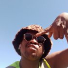 Man with Afro and sunglasses casting shadow, looking up against blue sky