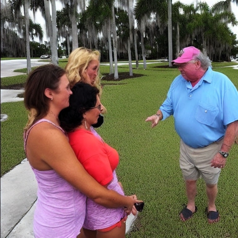 Four individuals conversing outdoors among palm trees and cloudy sky.