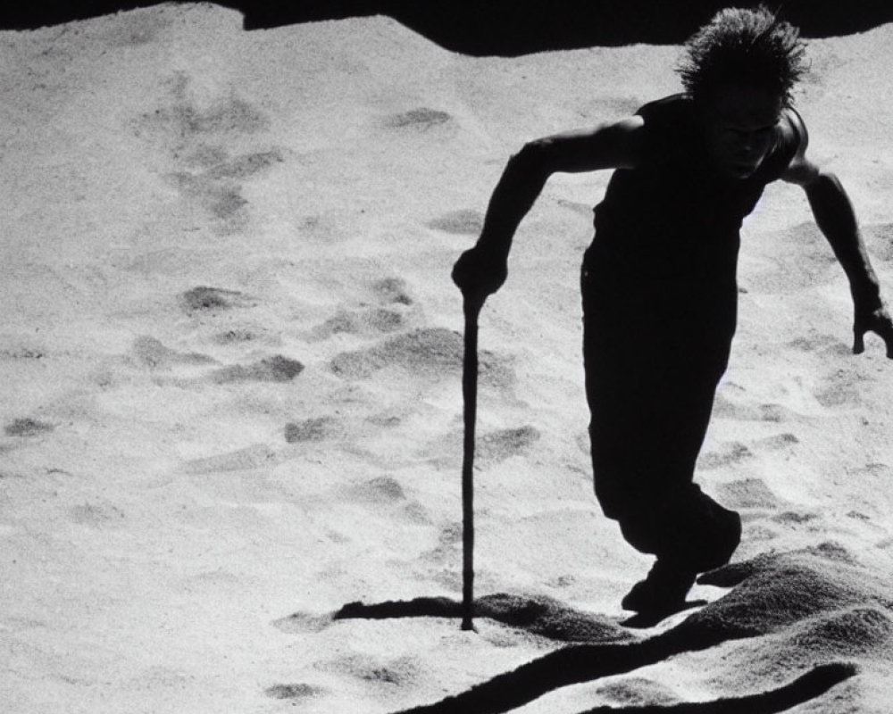 Spiky-haired person walking on sand with long shadow and stick