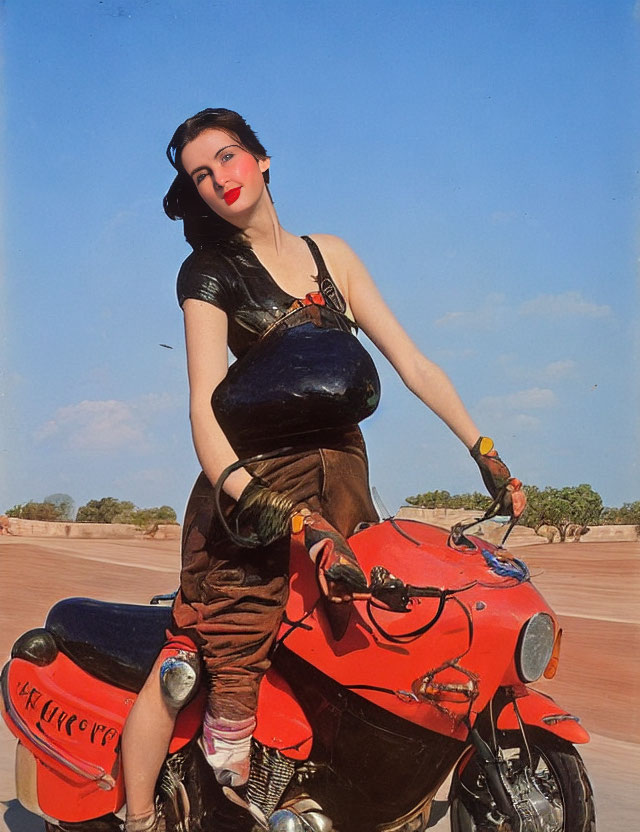 Person posing with red motorcycle in black top and brown trousers against blue sky