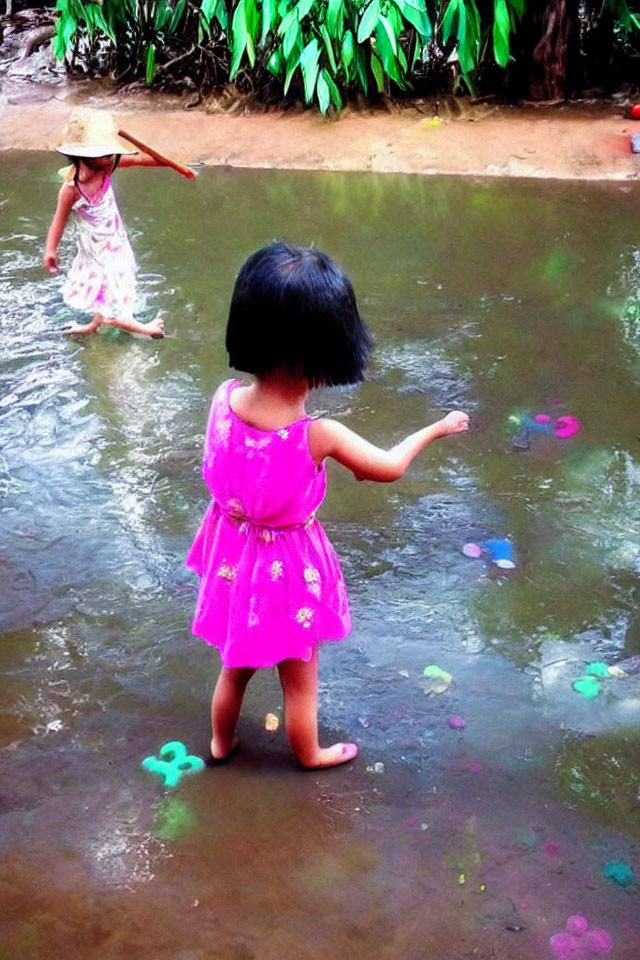 Young girls in pink dresses playing with water toys in outdoor stream