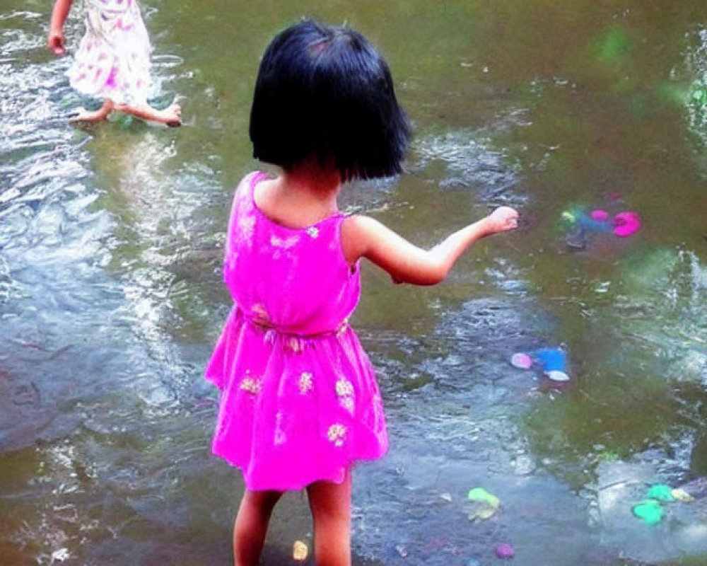 Young girls in pink dresses playing with water toys in outdoor stream