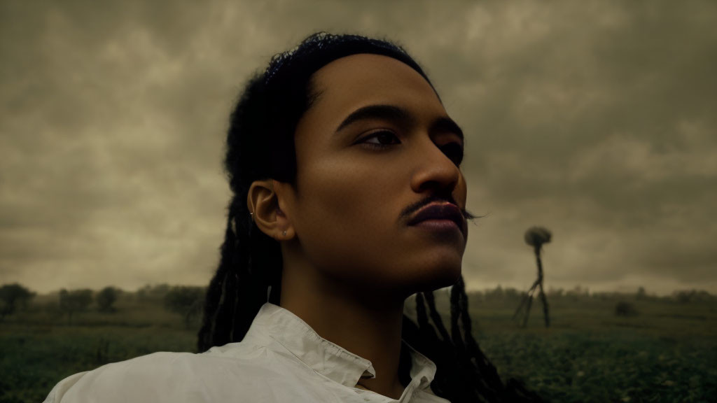 Person with dreadlocks in white shirt under stormy sky