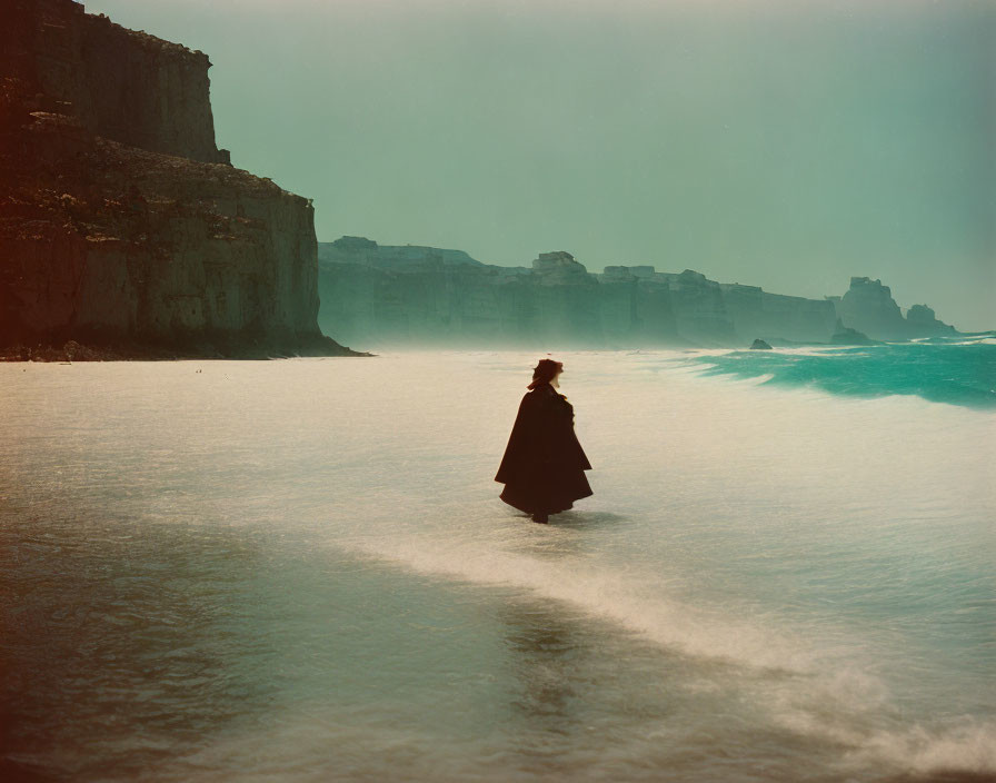 Mysterious figure in cloak on misty shoreline with cliffs